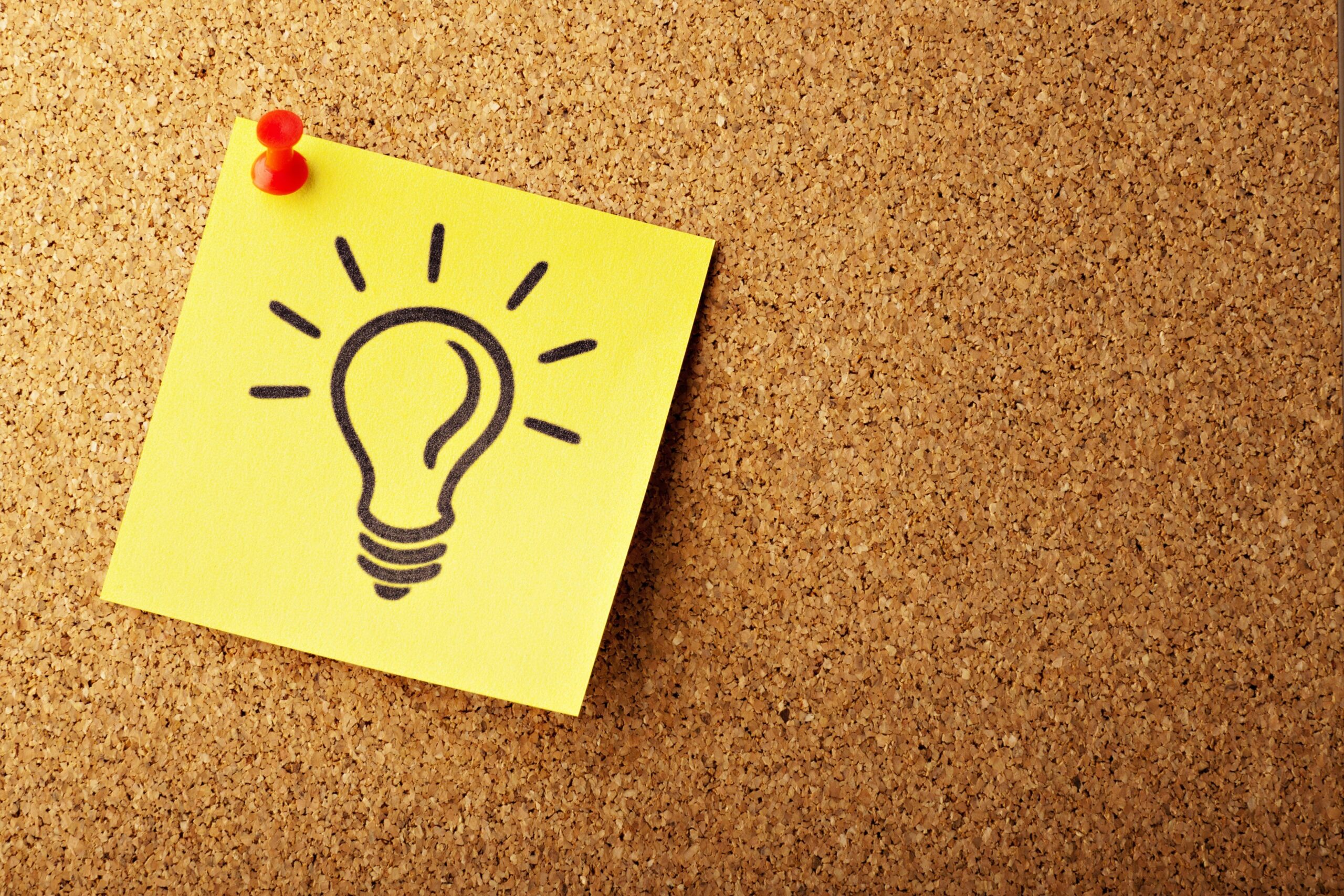 A yellow post-it note with a light bulb on it pinned to a cork board